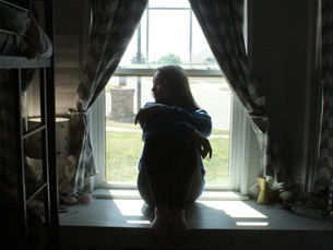 A teenage girl sits on a windowsill in a thoughtful pose
