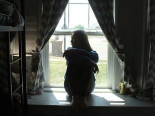 A teenage girl sits on a windowsill in a thoughtful pose